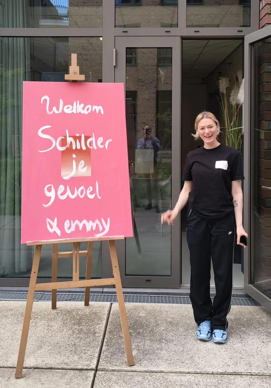 Kunstenaar Emmy naast een zelfgeschilderd welkomstbord